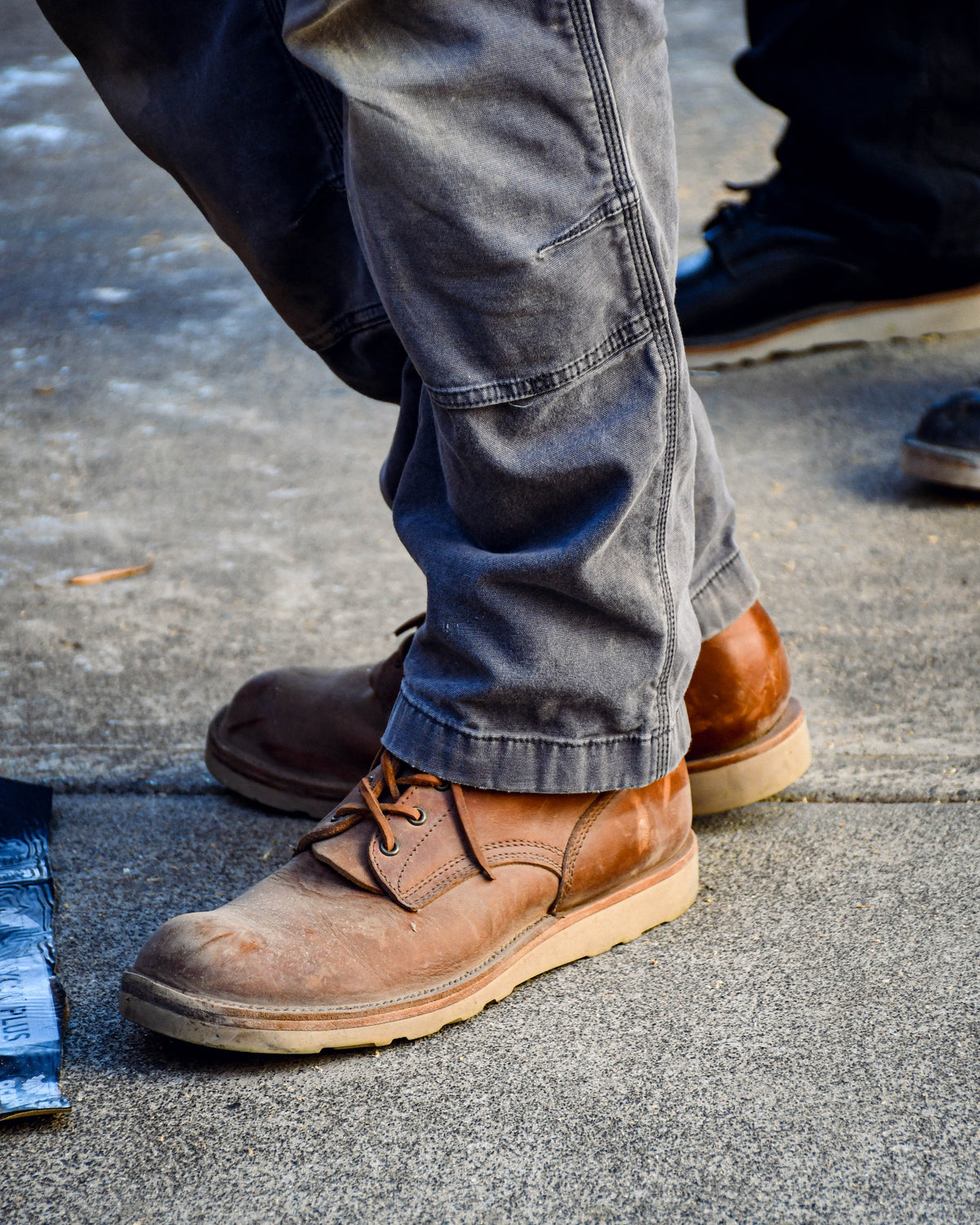 Model wearing brown leather boots and grey work pants standing on concrete.