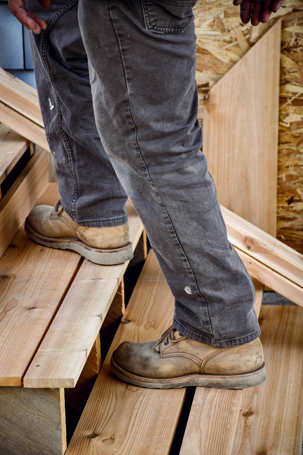 Model wearing tan sgb boots and grey work pants. He is walking up unfinished stairs.