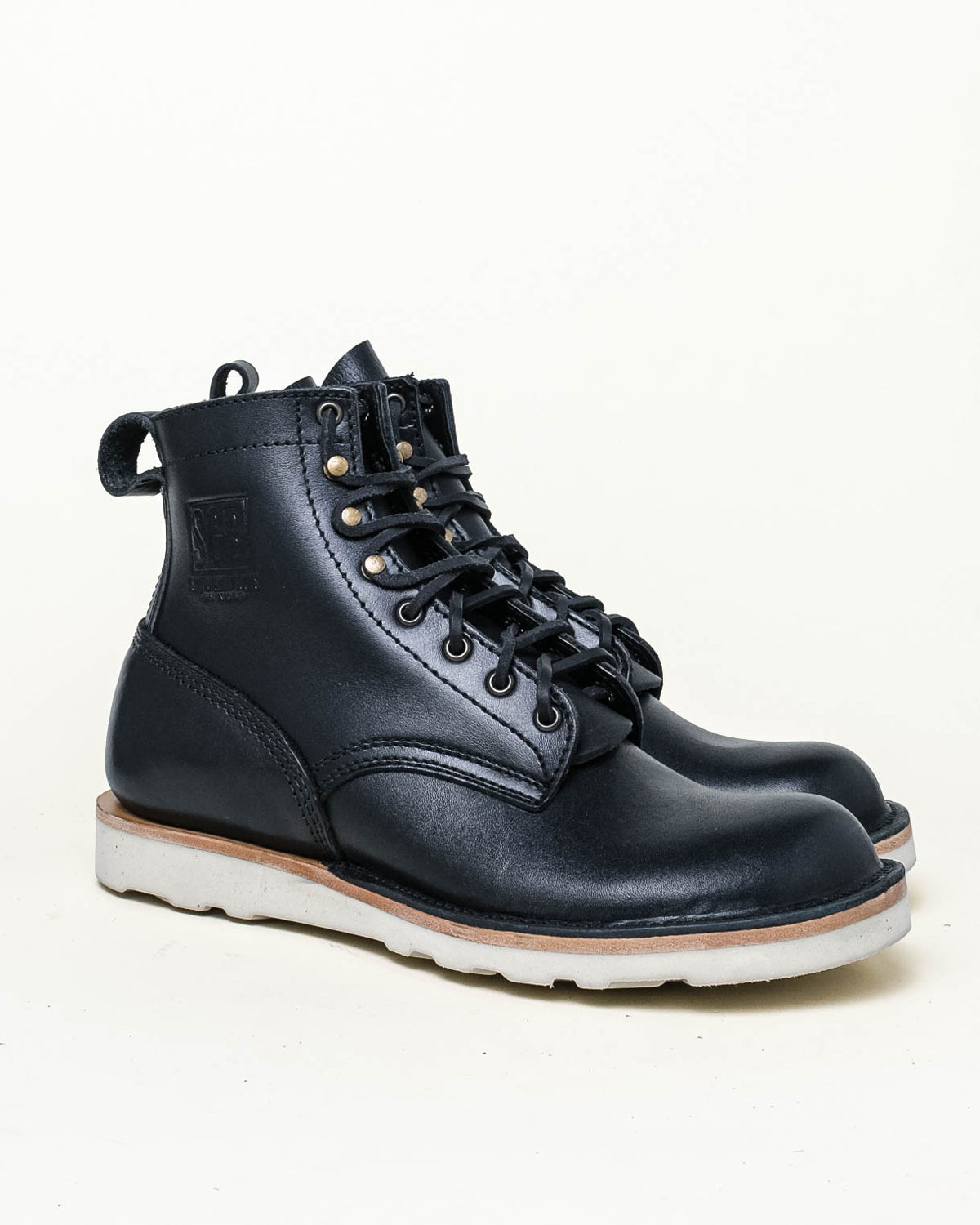 Black leather ankle boots with white wedge sole. Boots shown in 3-quarter profile in front of off white background. 
