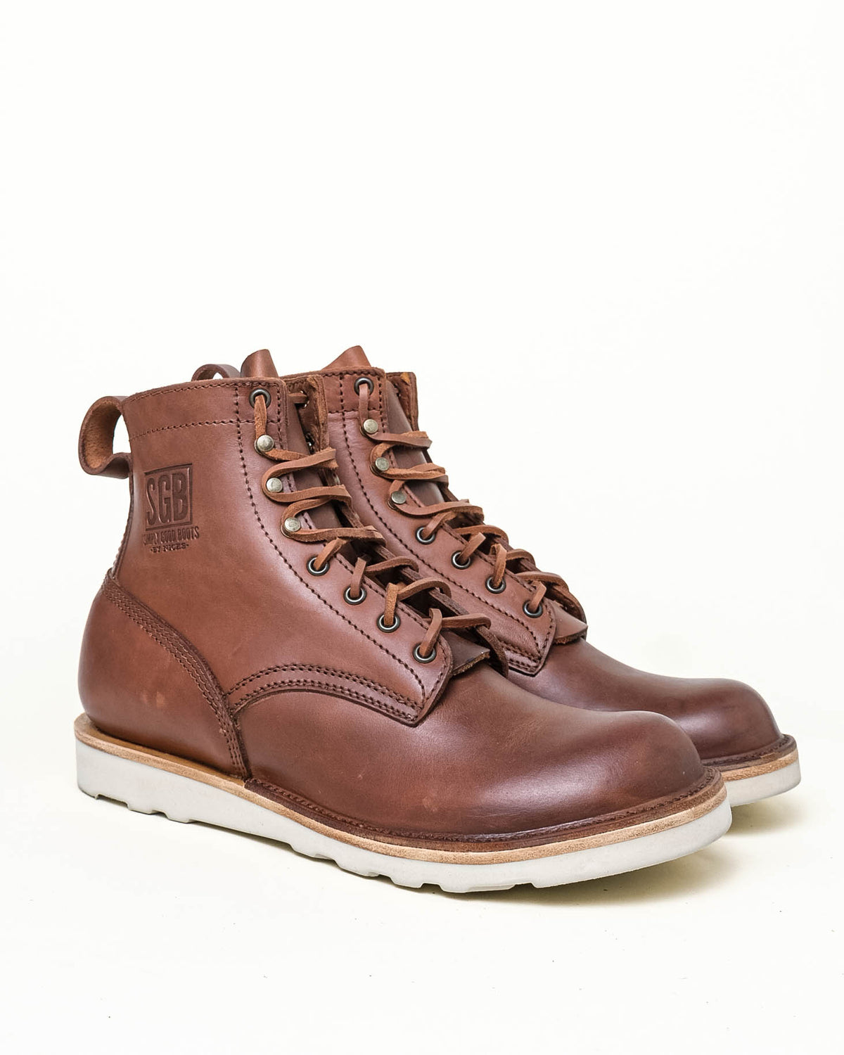 Brown leather ankle boots with white wedge sole, antiqued hardware and brown leather laces. Boots shown in 3-quarter profile in front of off white background.