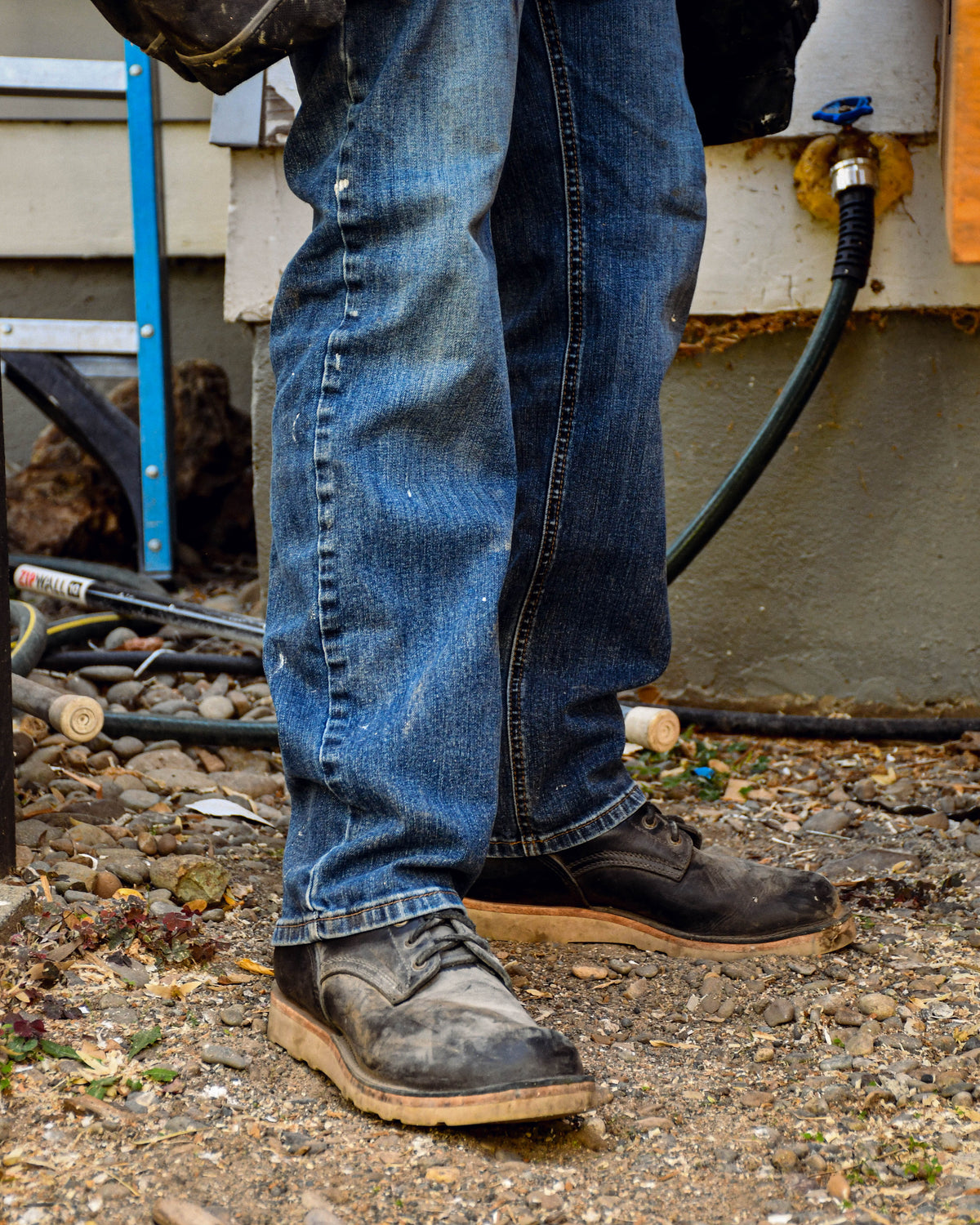 Model wearing dusty black leather boots and blue jeans standing in rocks.