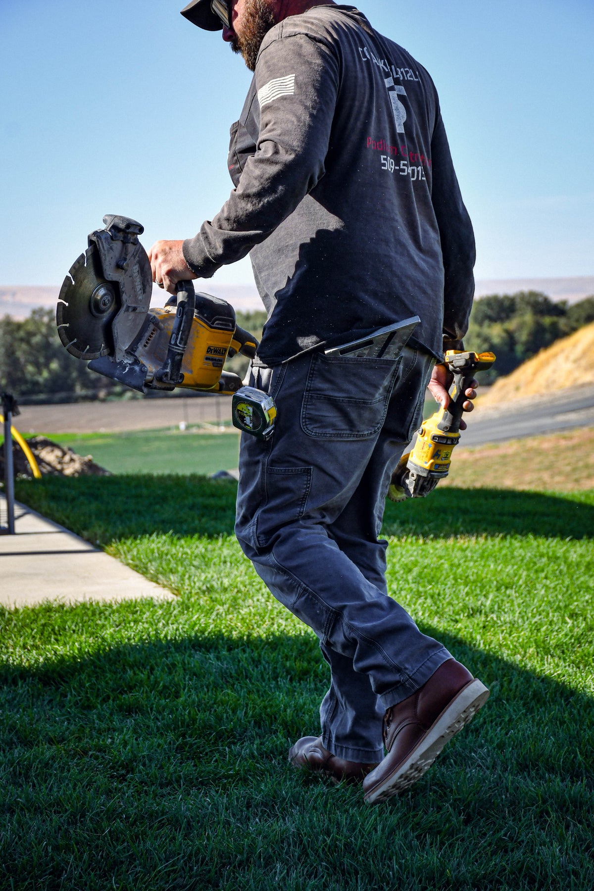 Model wearing brown leather boots walking through grass while holding power tools.