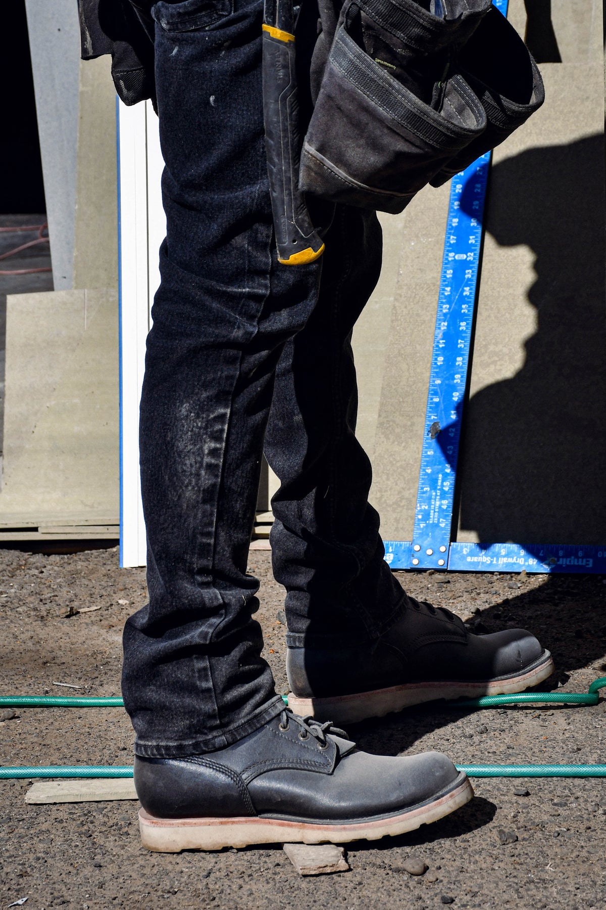 Model wearing black leather boots on job site. Standing on gravel and hoses while wearing tool belt. 